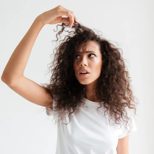 Woman with curly hair looking concerned, holding a strand . Hair Transplant Center Dallas TX